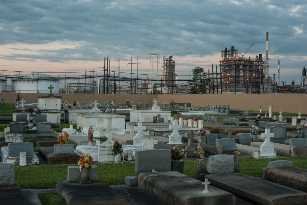 A petrochemical plant is seen on the horizon, looming over a graveyard in the foreground