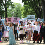 Trans youth, wearing colorful clothing and joyful expressions, march to the capitol holding signs reading