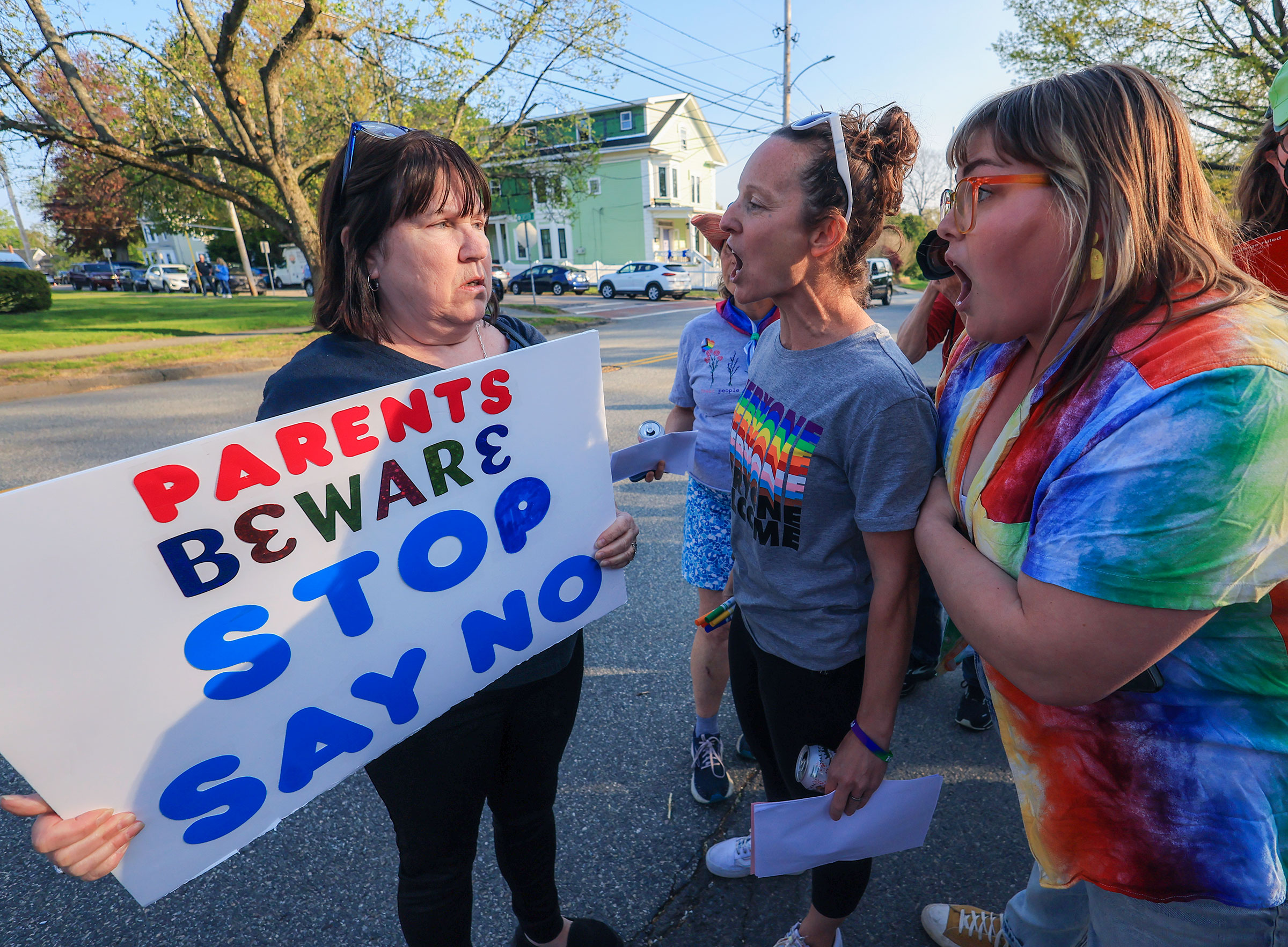 Two lgbtq+ allies speak with a woman holding a sign reading