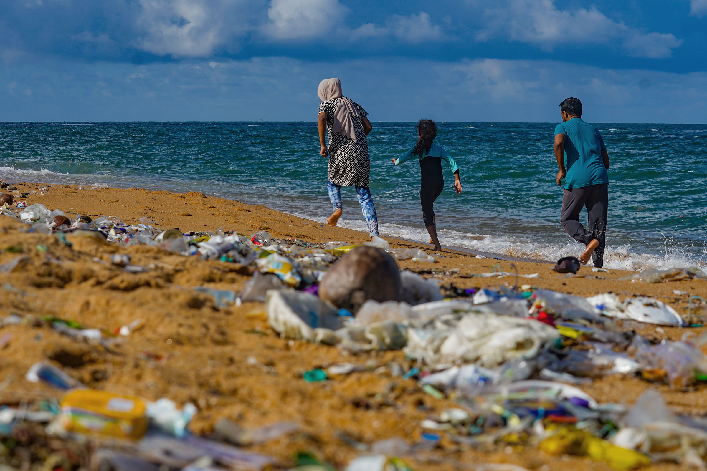 A family walk down what would be a beautiful beach were it not completely littered with plastic garbage