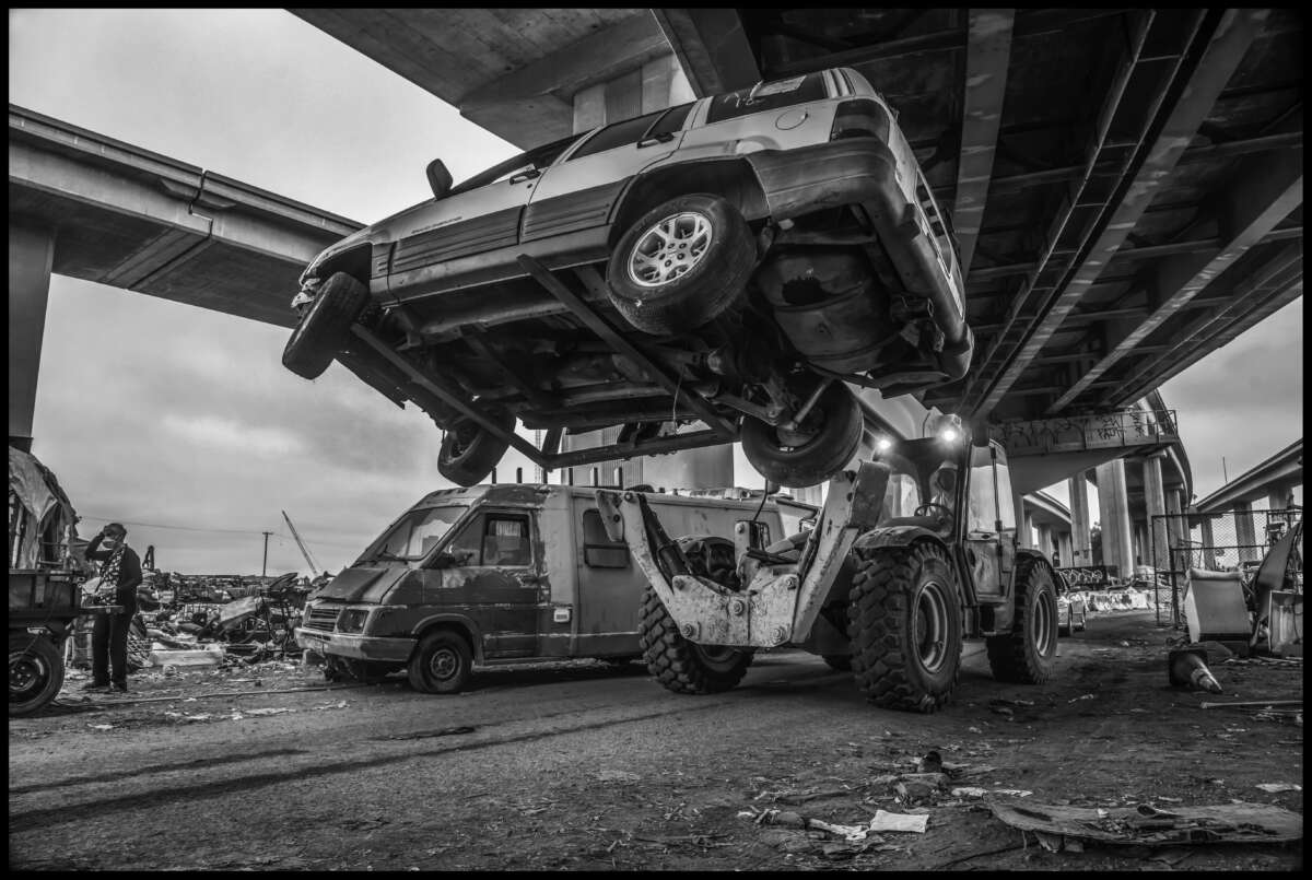 Sous le regard d'un résident, un chariot élévateur hisse son SUV et le sort du camp sous l'autoroute.