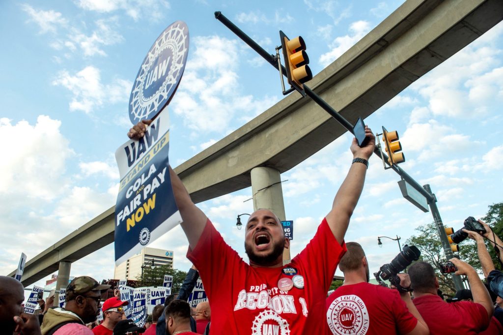 A man raises a sign with arms outstretched that reads