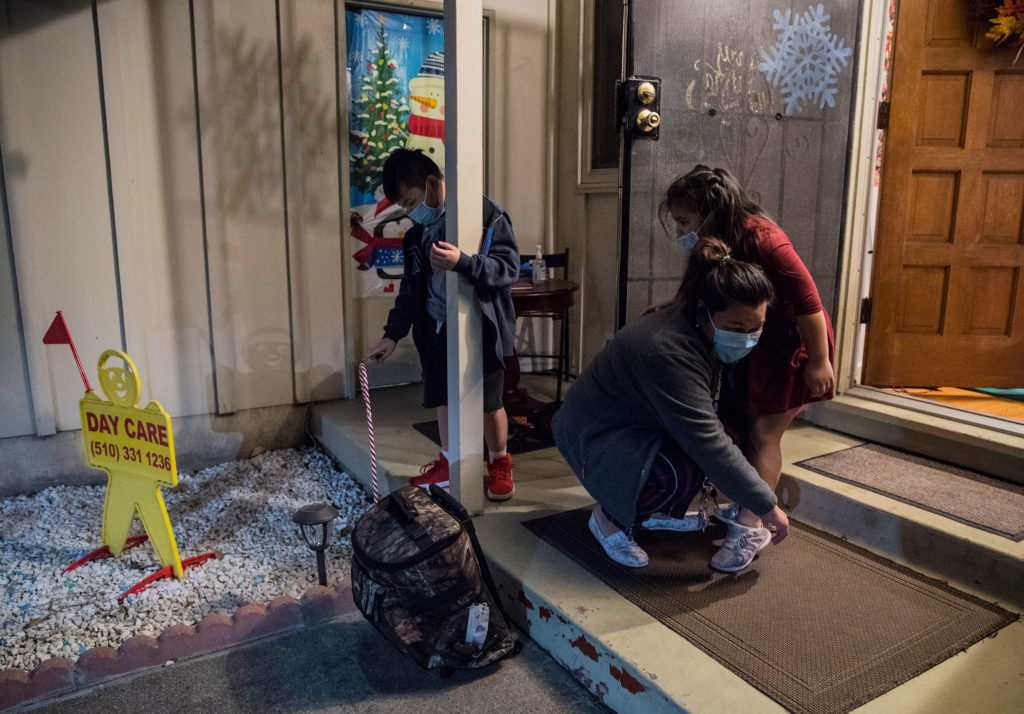 A mother helps her child put on shoes outside of a daycare center