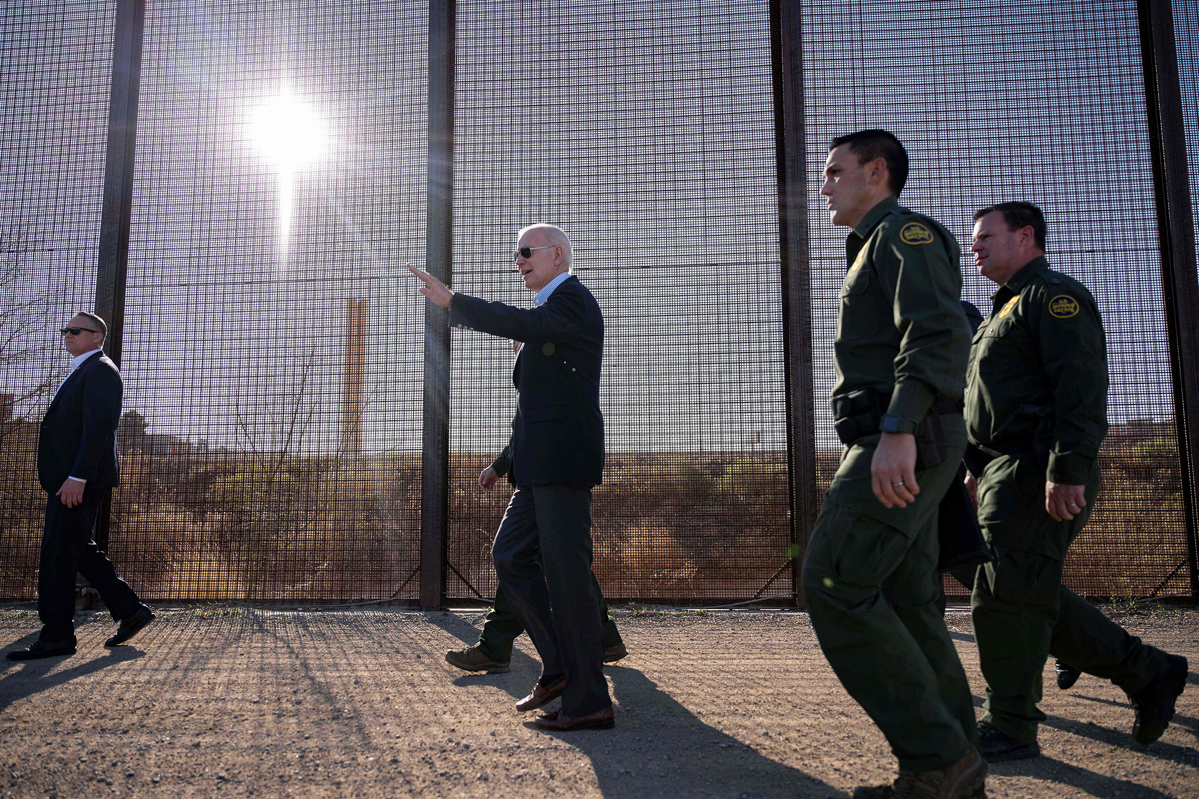 Joe Biden walks alongside border patrol agents and beside the us/mexio border fence