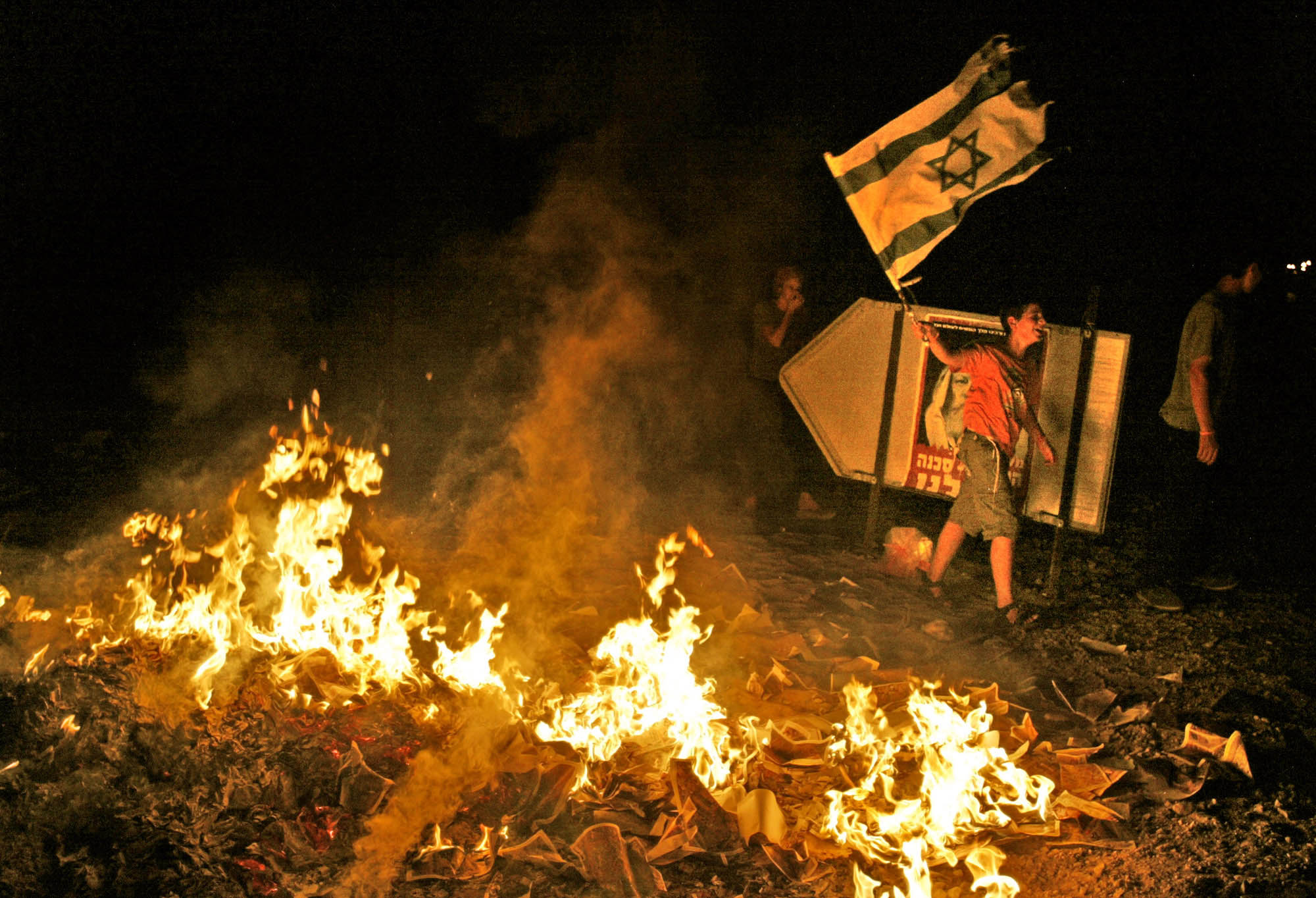 A Jewish protestor waves the Israeli flag next to a bonfire started by a mob who looted the back of a passing vehicle loaded with maps of the Gaza Strip in front of the Neve Dekalim settlement in the Gaza Strip on August 14, 2005.