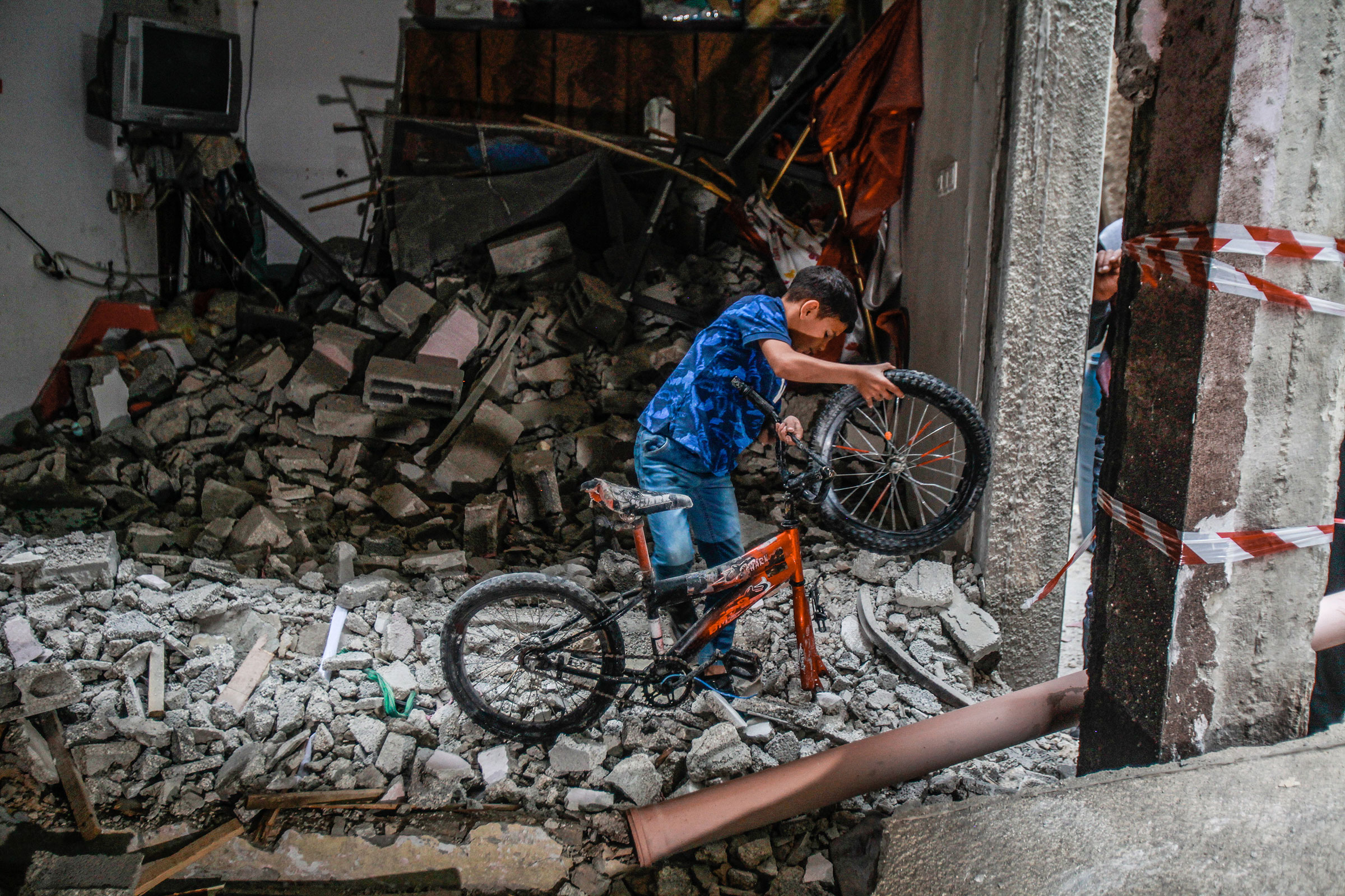 A child pulls his destroyed bike out of rubble that was once an apartment