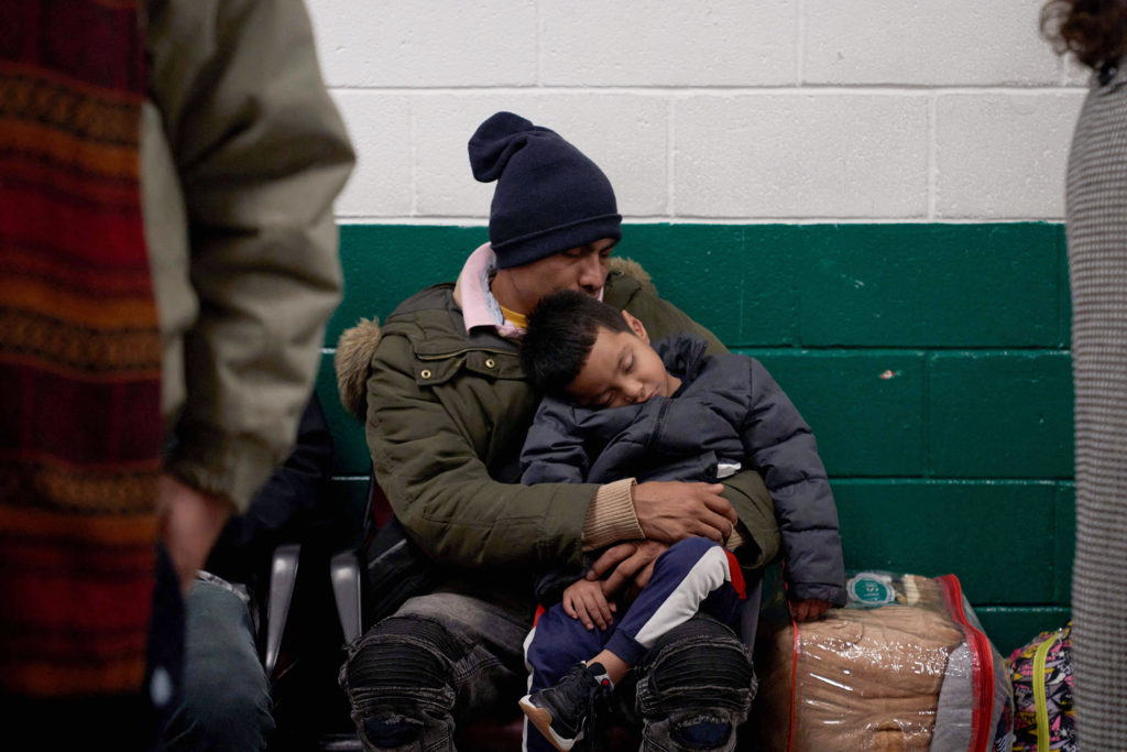 A man holds his sleeping son as they wait in a bus station