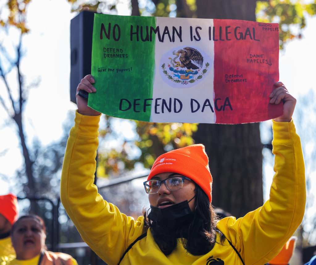 A protester chants while holding a sign fashioned after the Mexican flag that reads: NO HUMAN IS ILLEGAL; DEFEND DACA