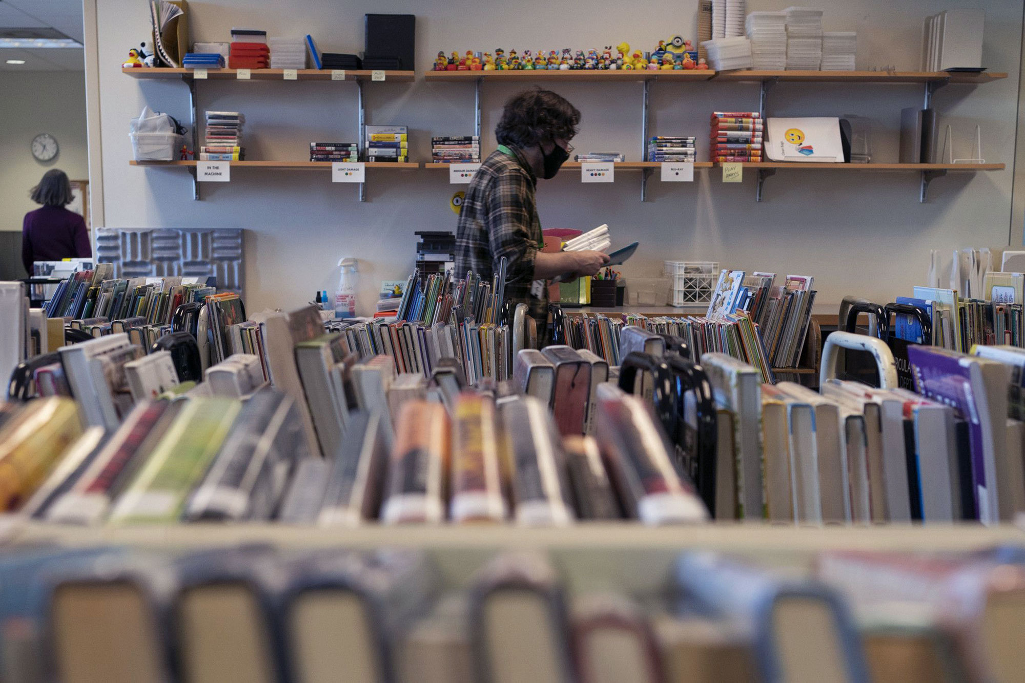 A masked library worker walks among books