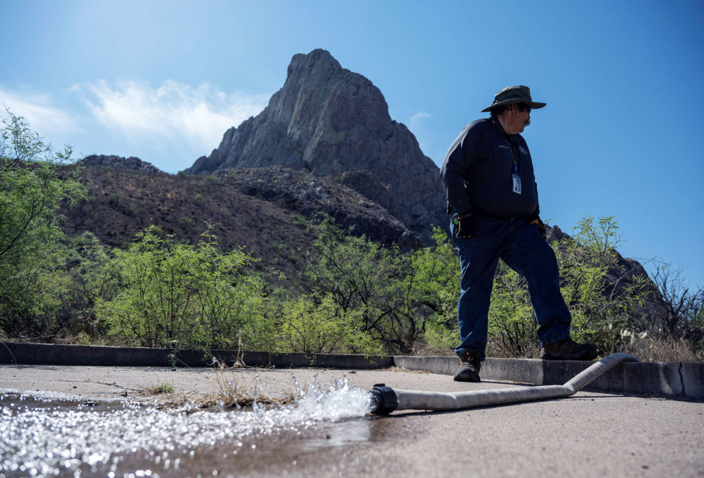 A ranger stands by a hose as it sputters water onto the ground