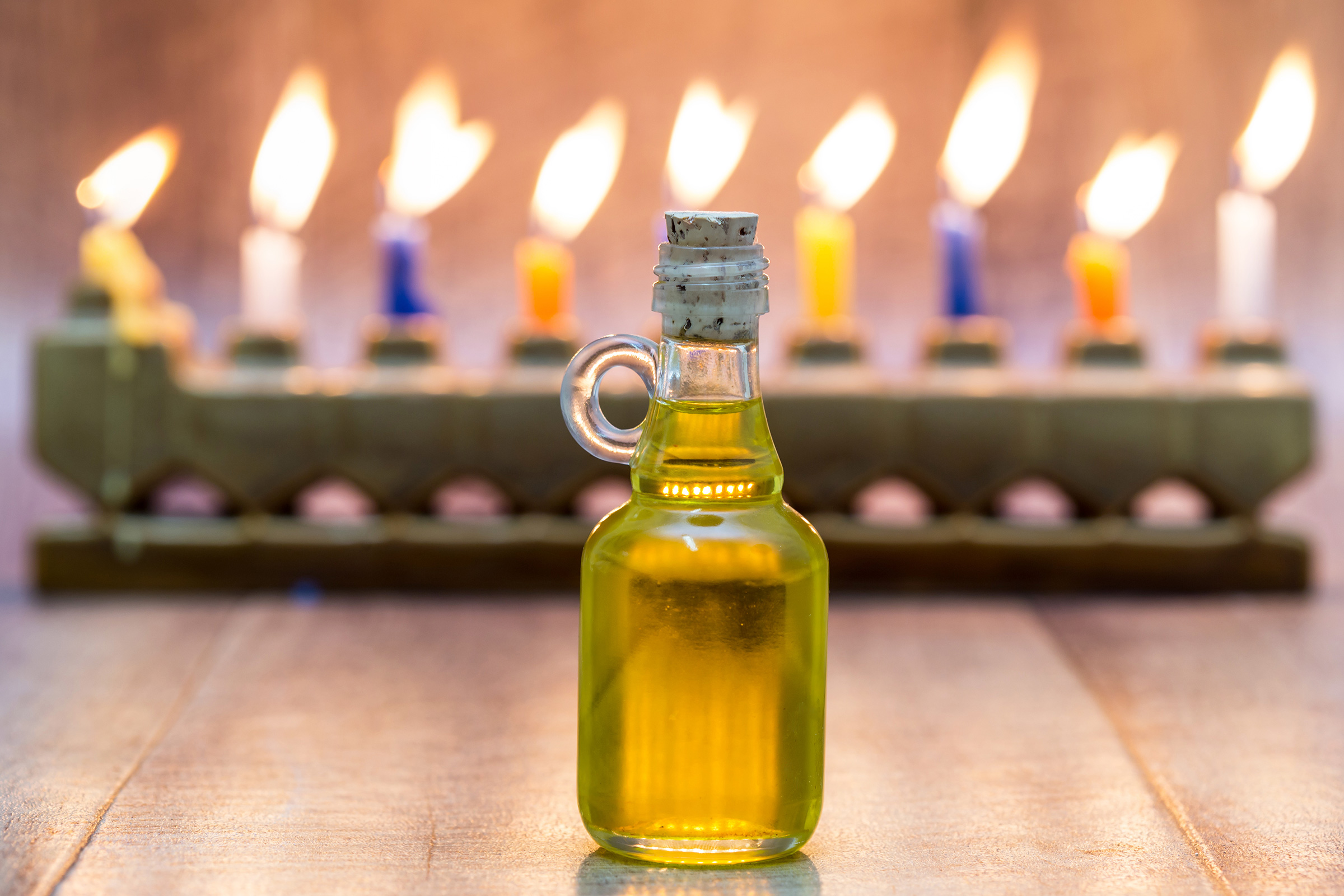 A lit menorah is seen behind an in-focus bottle of oil