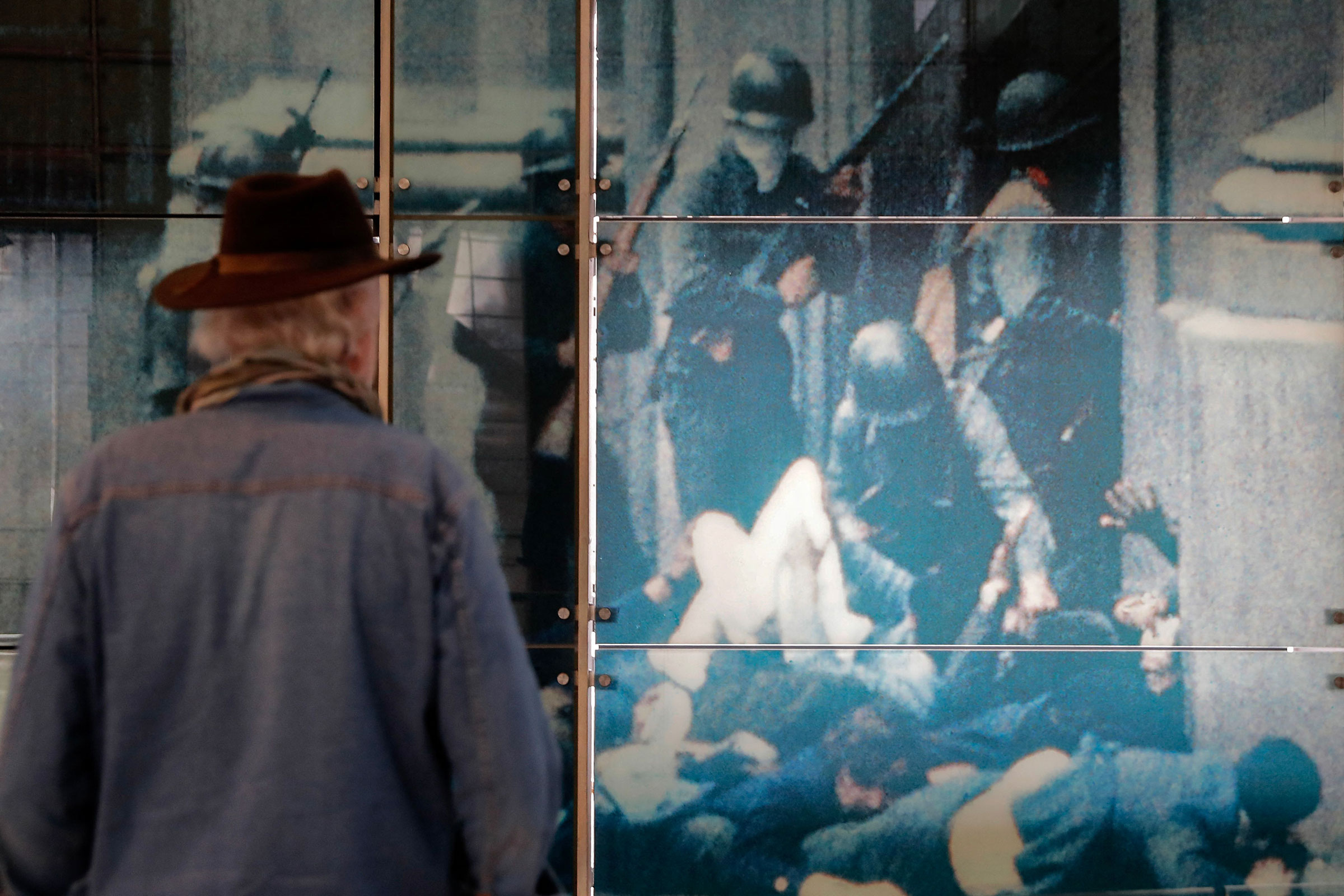 A man, his back facing the viewer, gazes at a photo he shot of the Chilean Coup of 1974