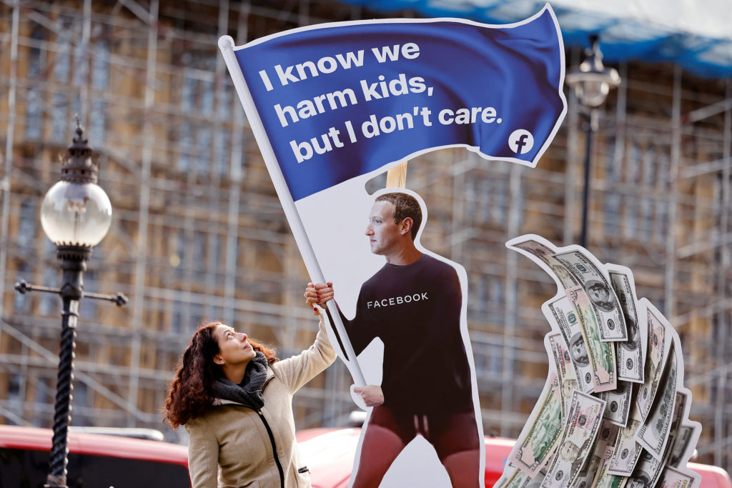 an art installation of mark zuckerberg holding a flag reading "I know we harm kids, but I don