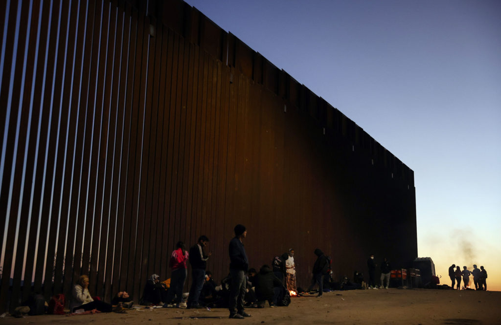 People cook food on an open fire by the US/Mexico border fence