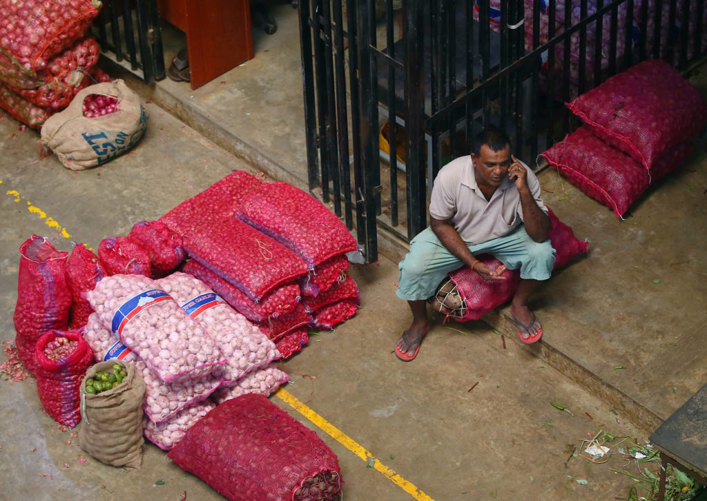 A vendor speaks to someone on the phone while seated next to large bags of produce for sale