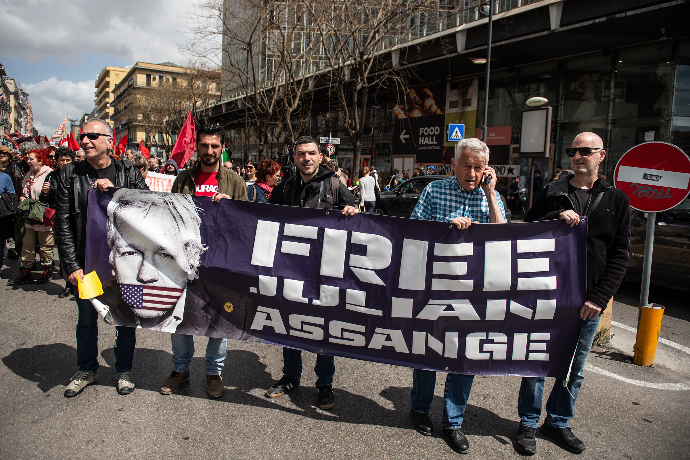 People march behind a banner displaying the face of Julian Assange alongside the words