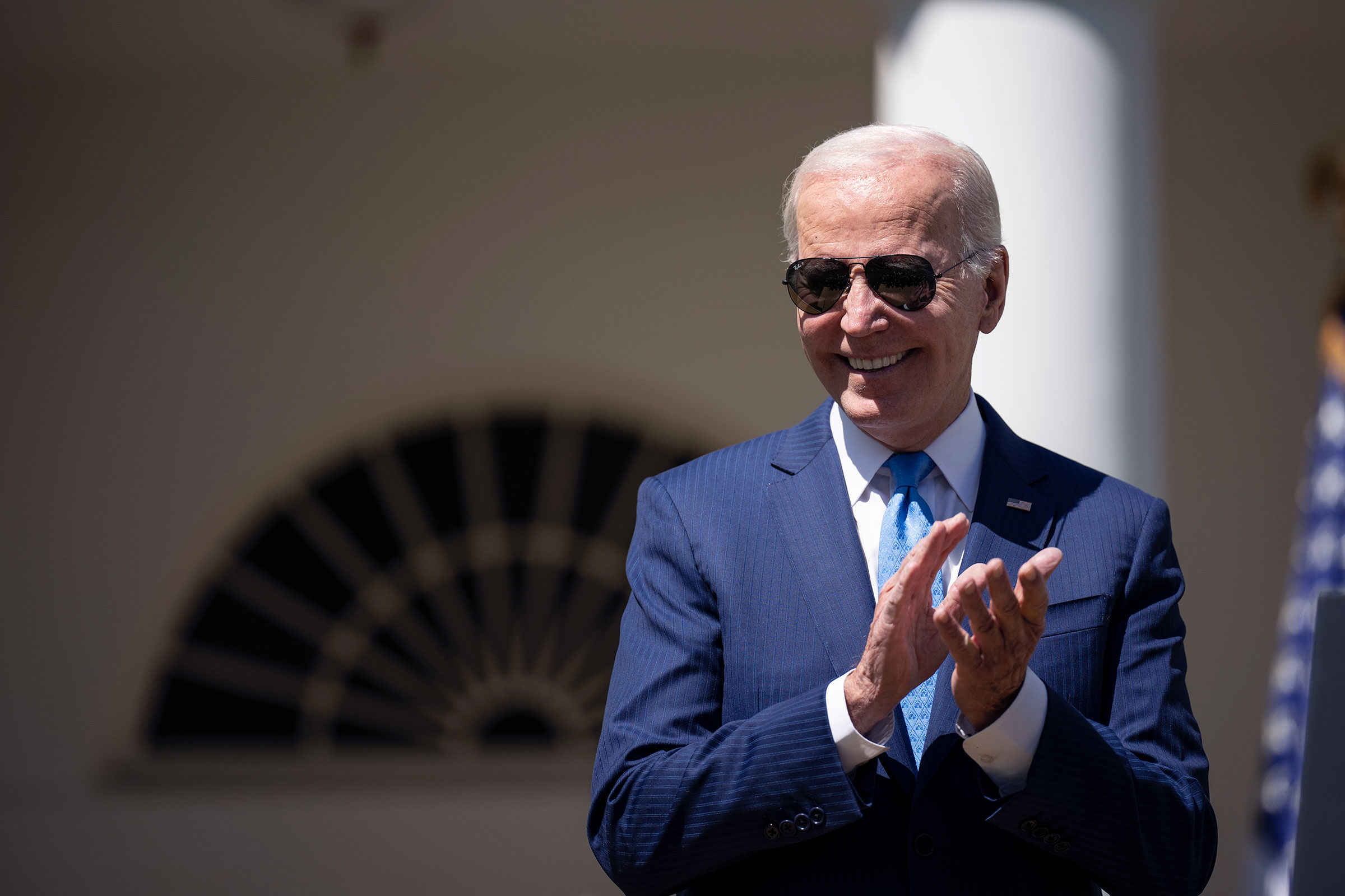 Joe Biden claps while wearing aviator sunglasses.