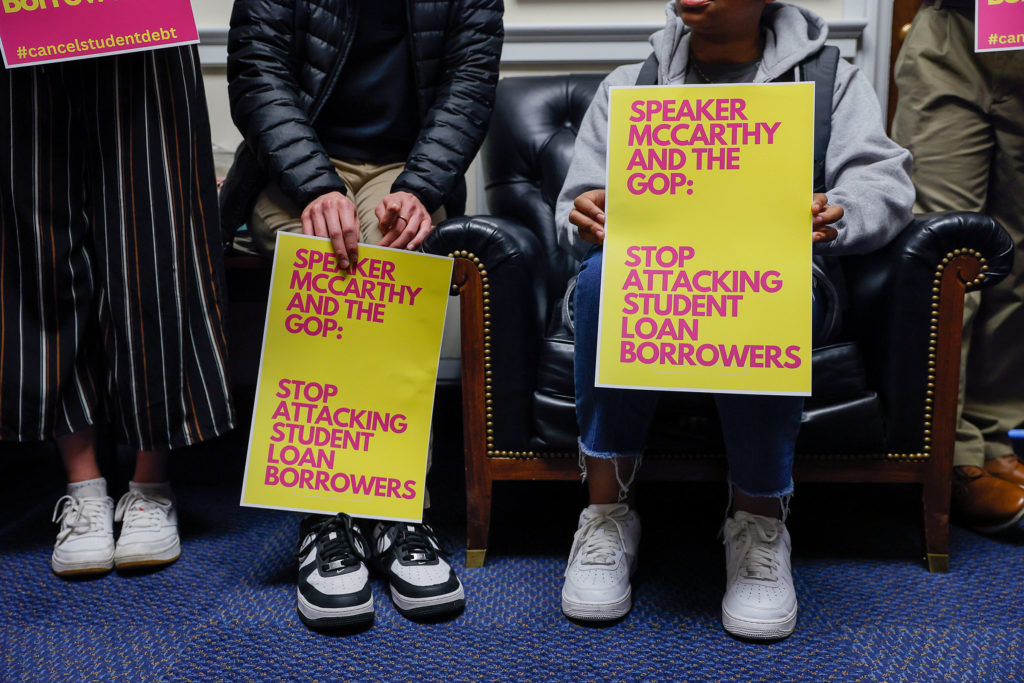 People sit while holding signs reading