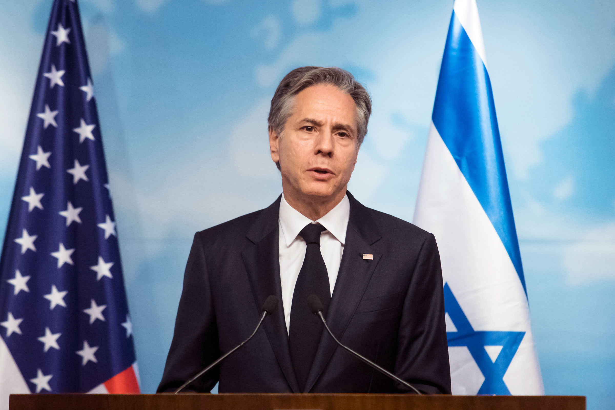 Antony Blinken stands in front of U.S. and Israeli flags while delivering a speech