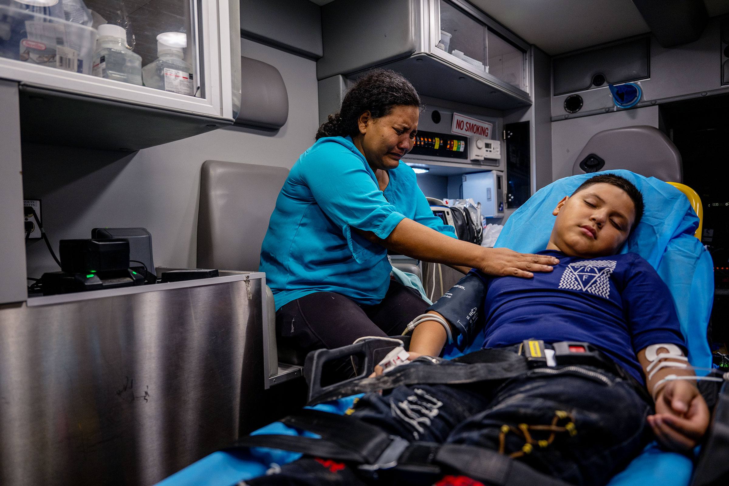 A mother cries beside her unconscious child in the back of an ambulance