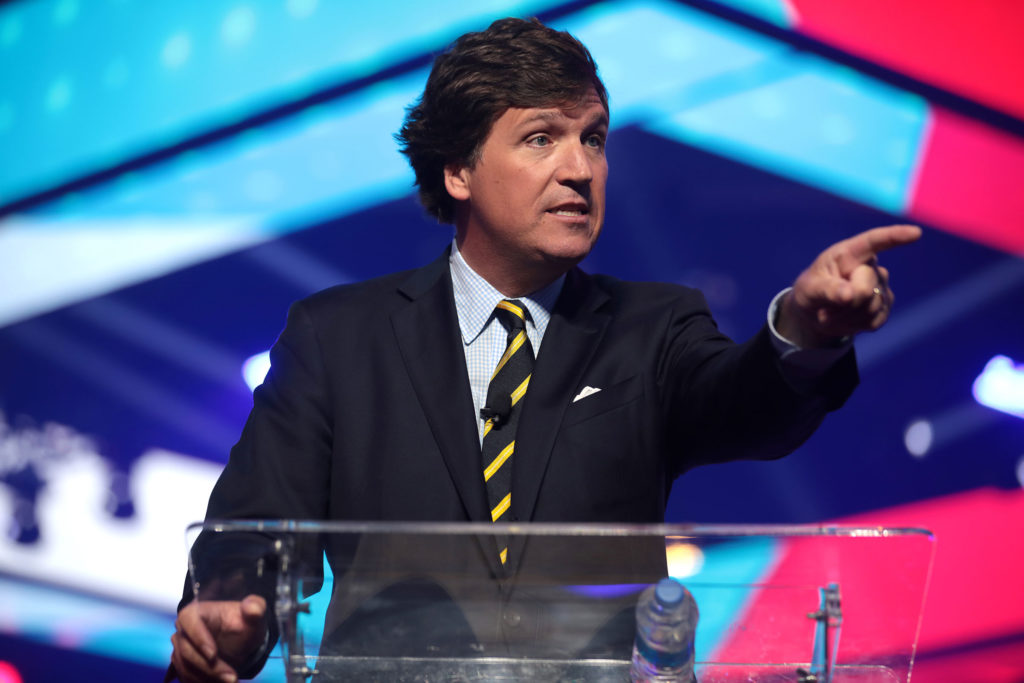 Tucker Carlson points outward while speaking at a podium
