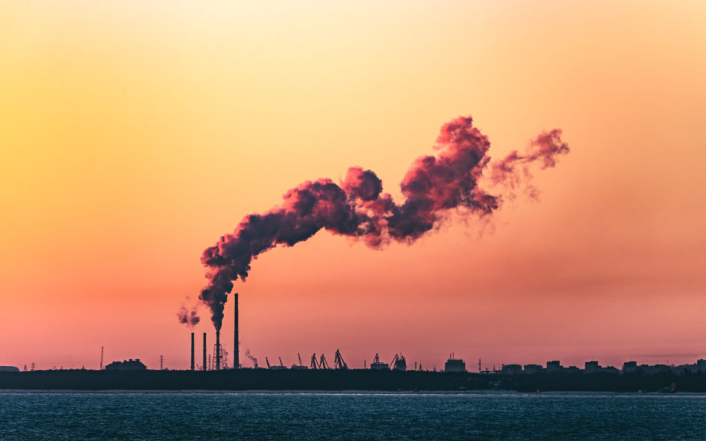 Smoke emissions are pictured over a body of water and sunset