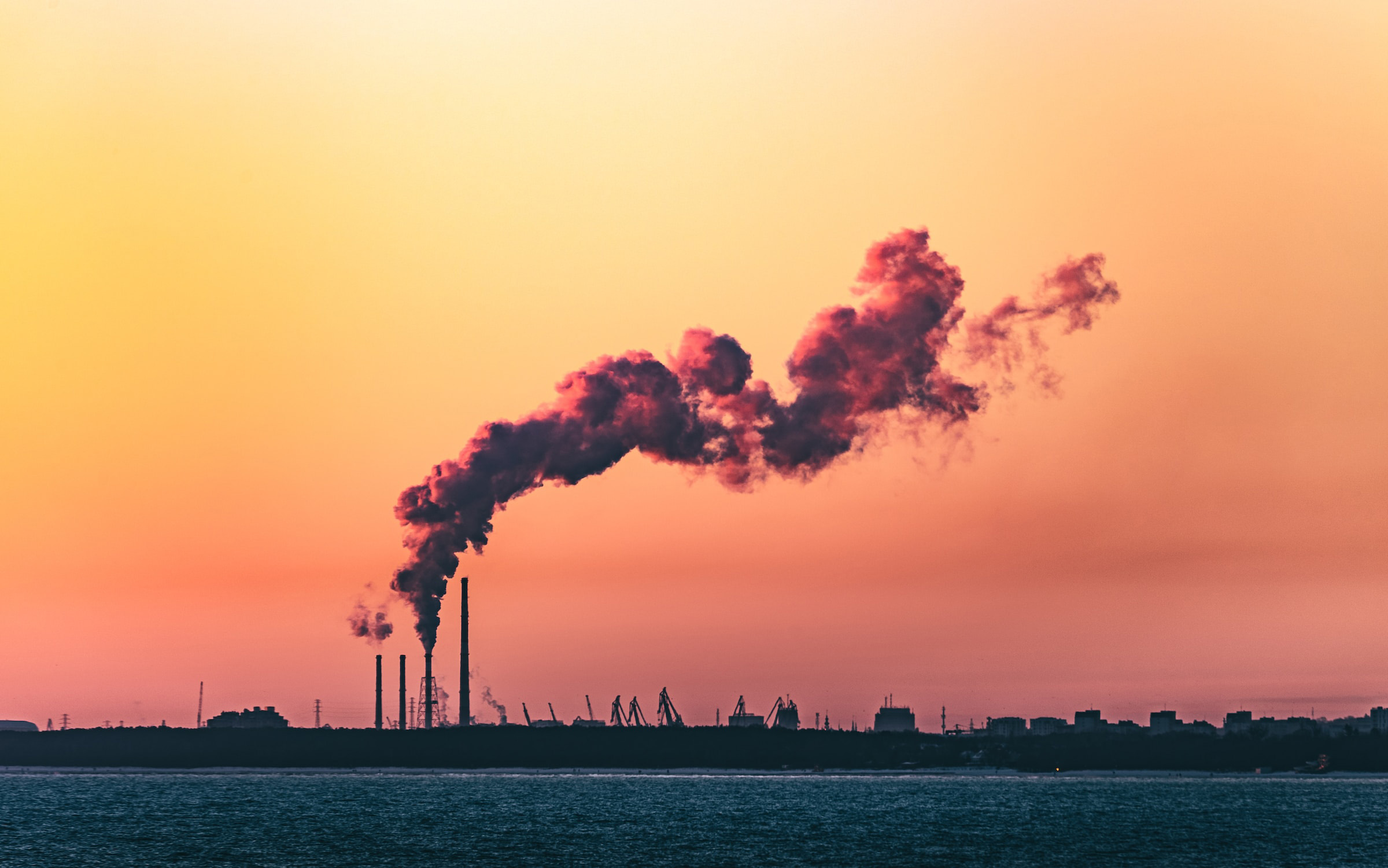 Smoke emissions are pictured over a body of water and sunset