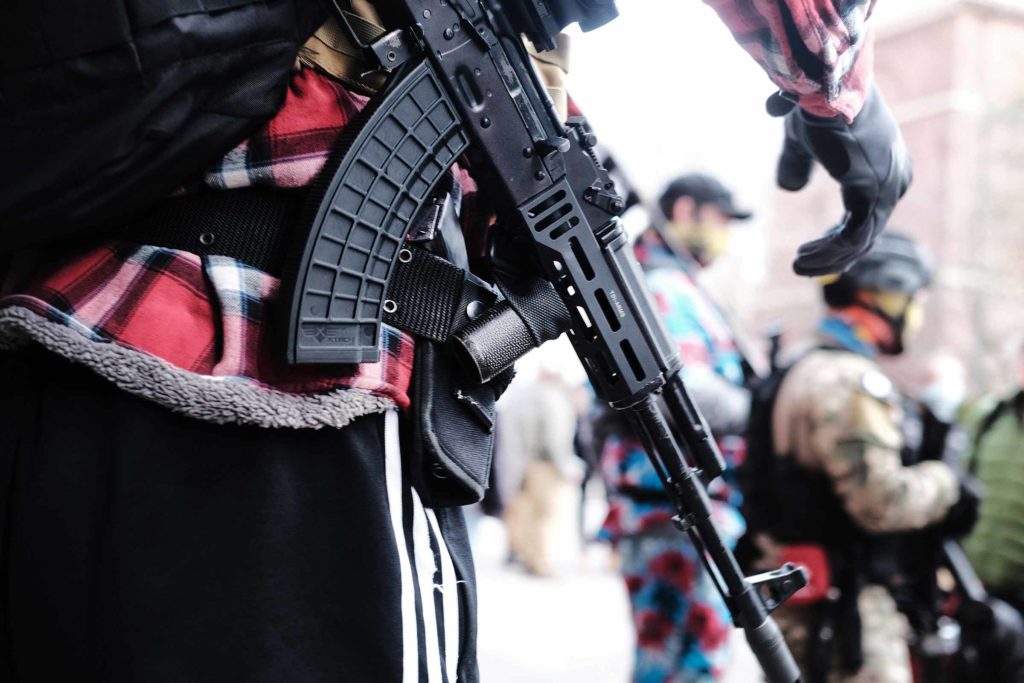 A man carrying an assault rifile stands near other men carrying assault rifles during an outdoor