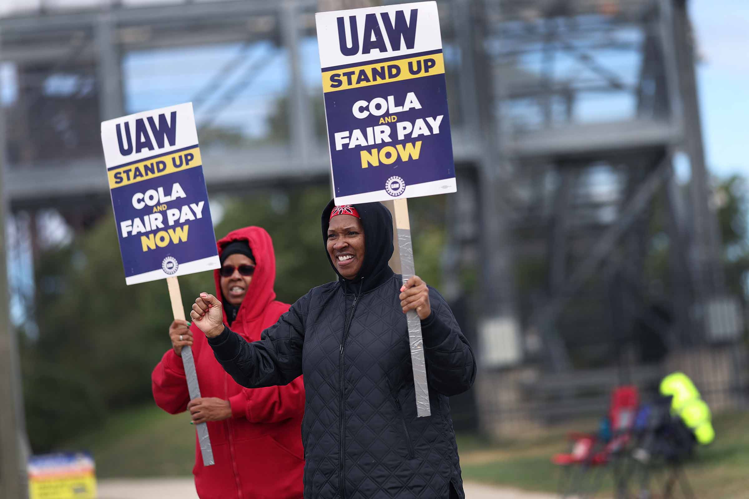 Two strikers stand outside holding signs reading