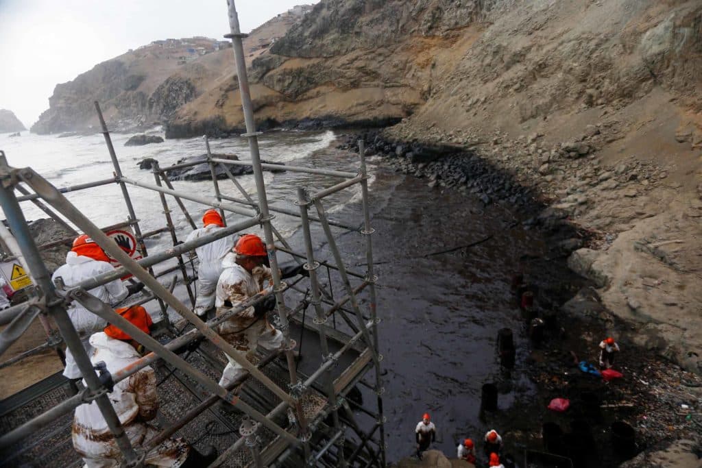 People in protective gear and red helmets clean up an oil spill