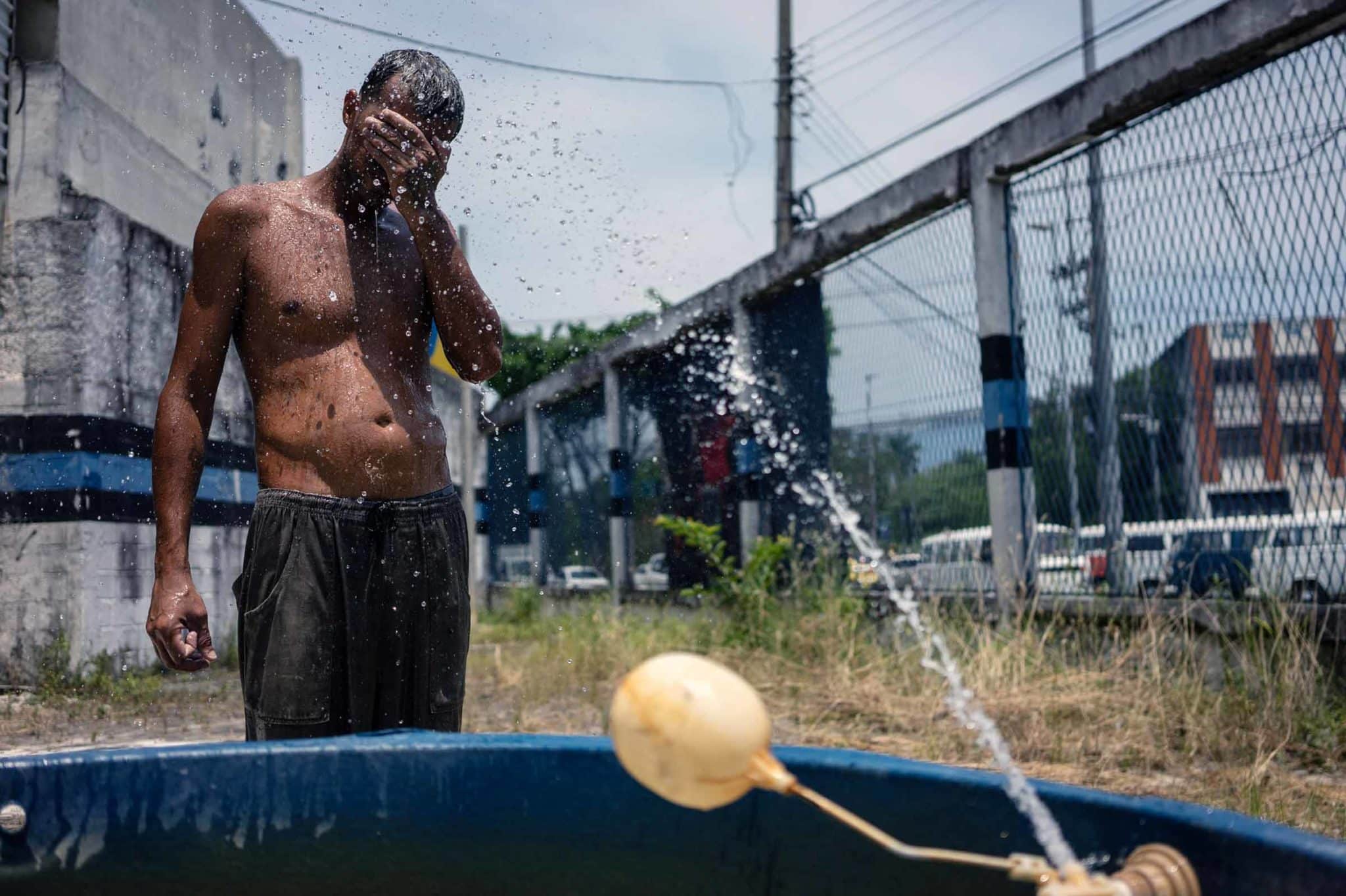 A man covers his face while a makeshift sprinkler sprays him with water