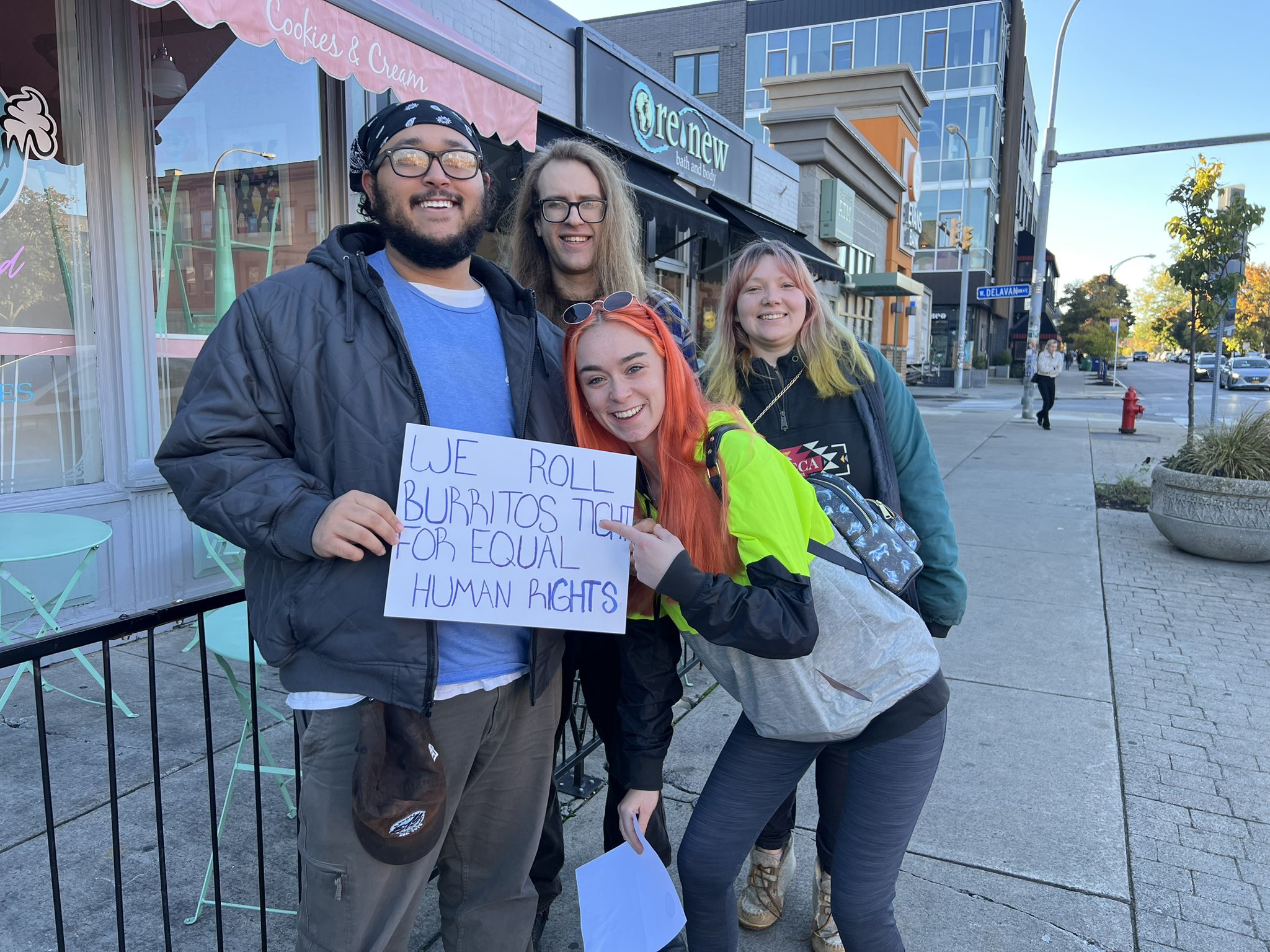 People stand outside of a restaurant to deliver an addressPeople pose for a photo around a sign that reads