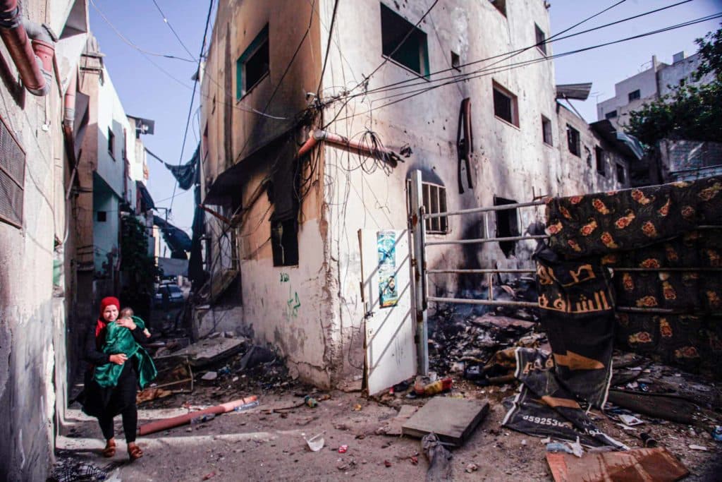 A woman carries a baby through a rubble-strewn street