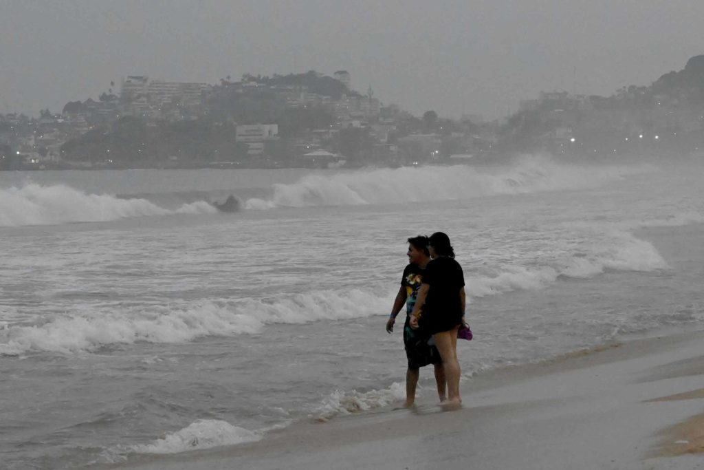 People stand on a beach as a storm kicks up waves