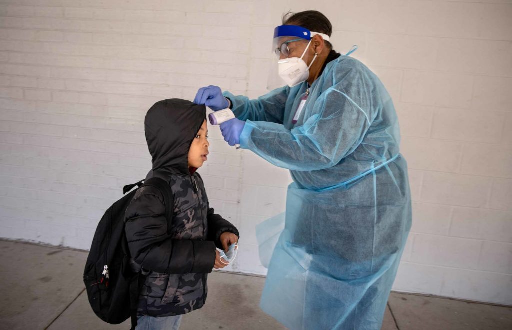 A school nurse in ppe takes a student