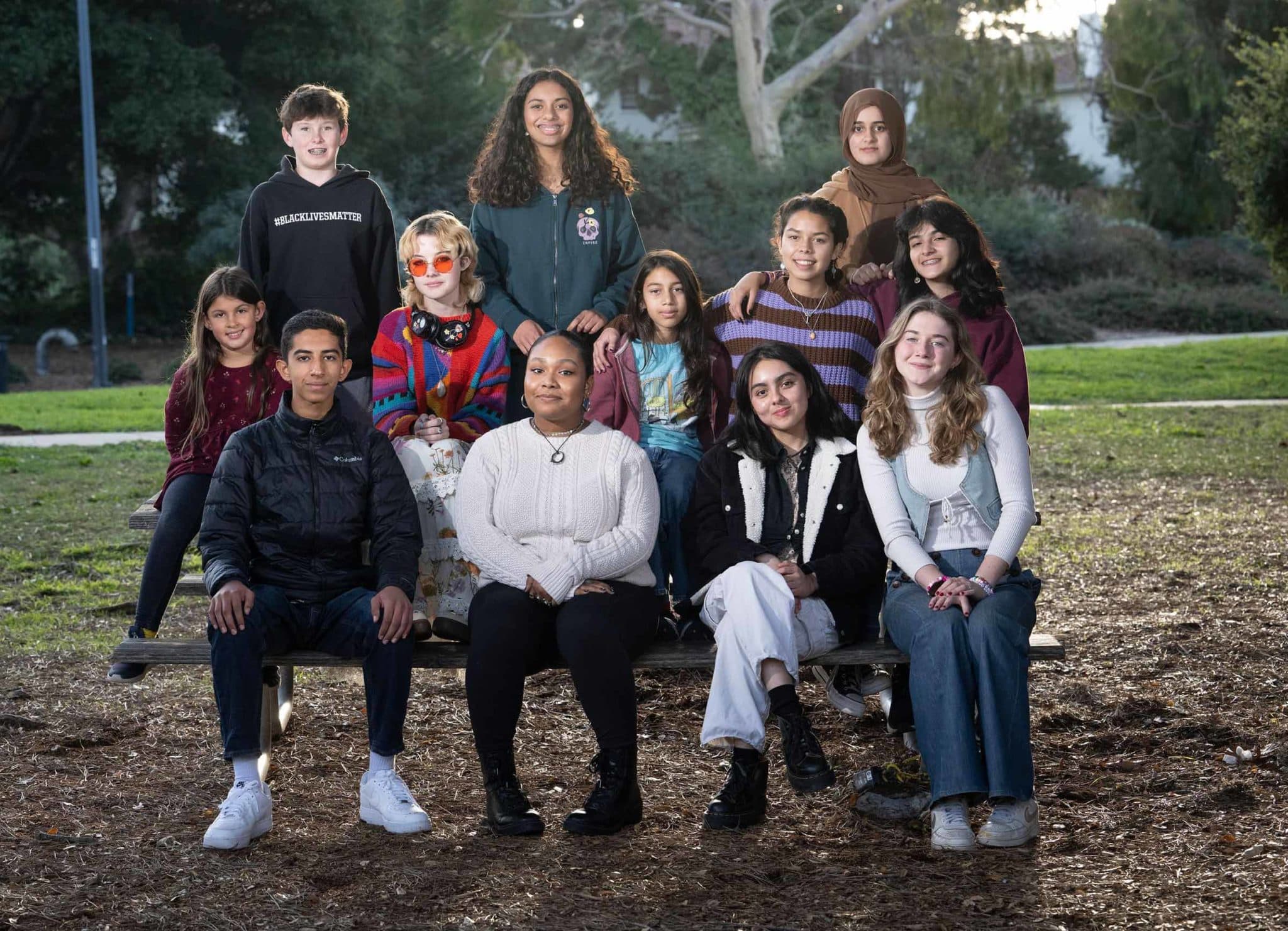 A group of kids gather on a park bench for an outdoor photo