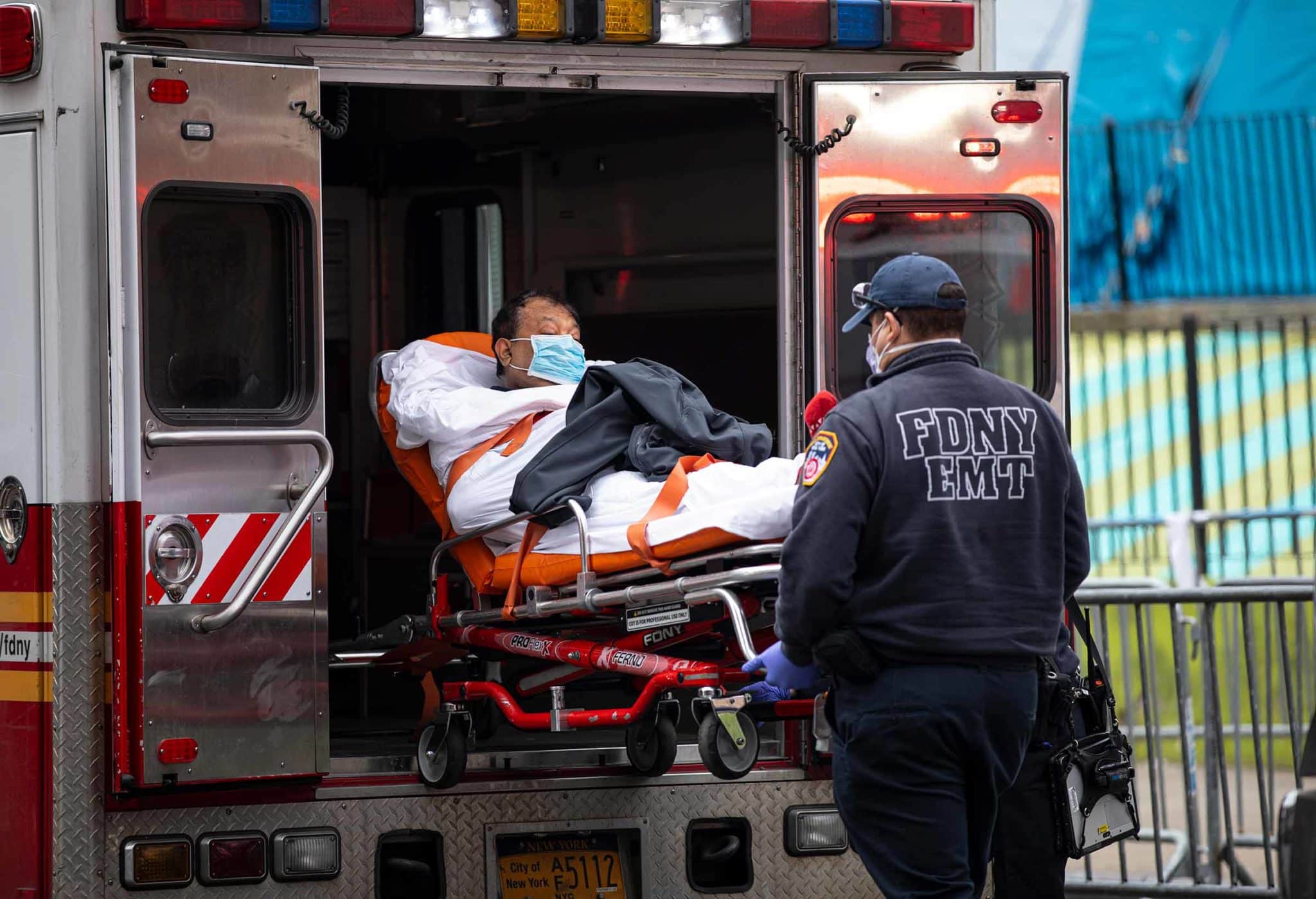 A man on a gurney is wheeled either into or out of an ambulance by paramedics