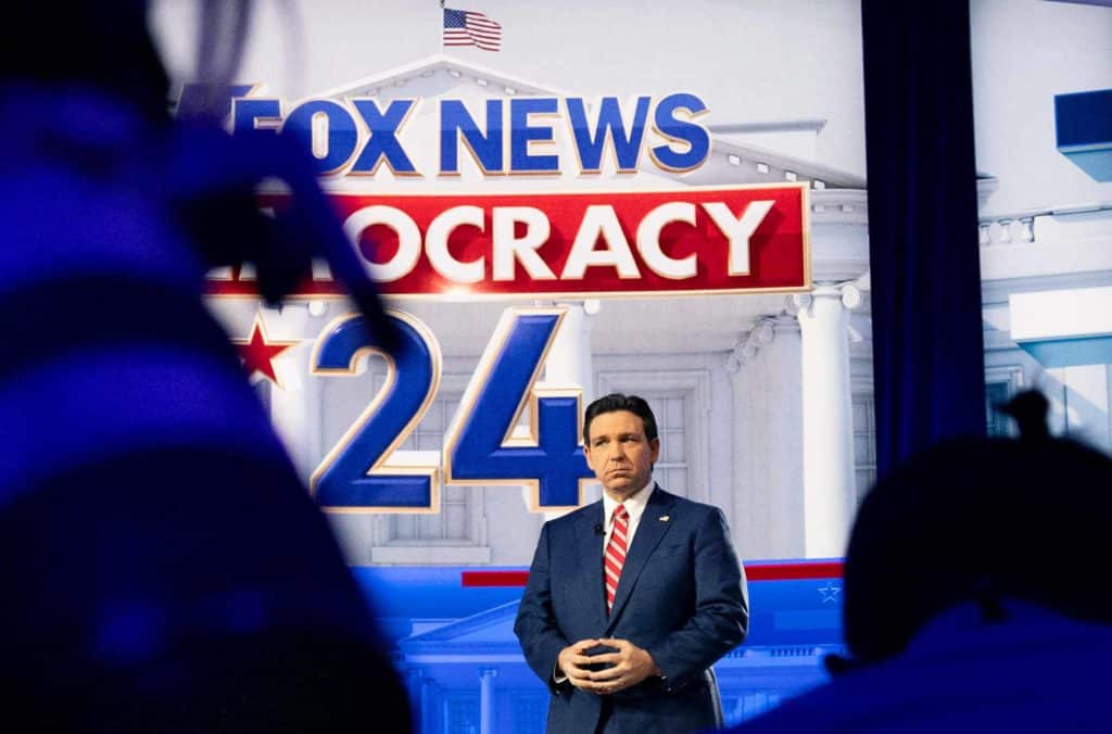 Ron DeSantis stands underneath a sign reading