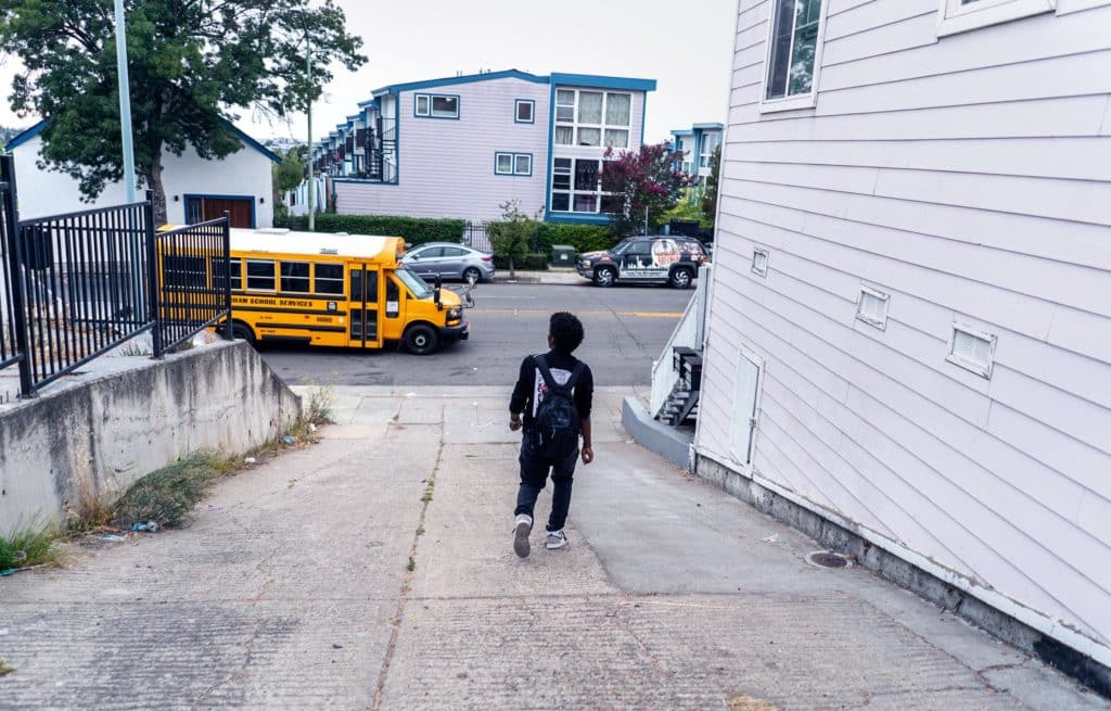 A student walks to the yellow school bus waiting for him at the end of his driveway