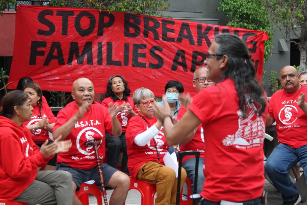 Members of the Hillside Villa Tenants Association clap and chant in front of a banner which says