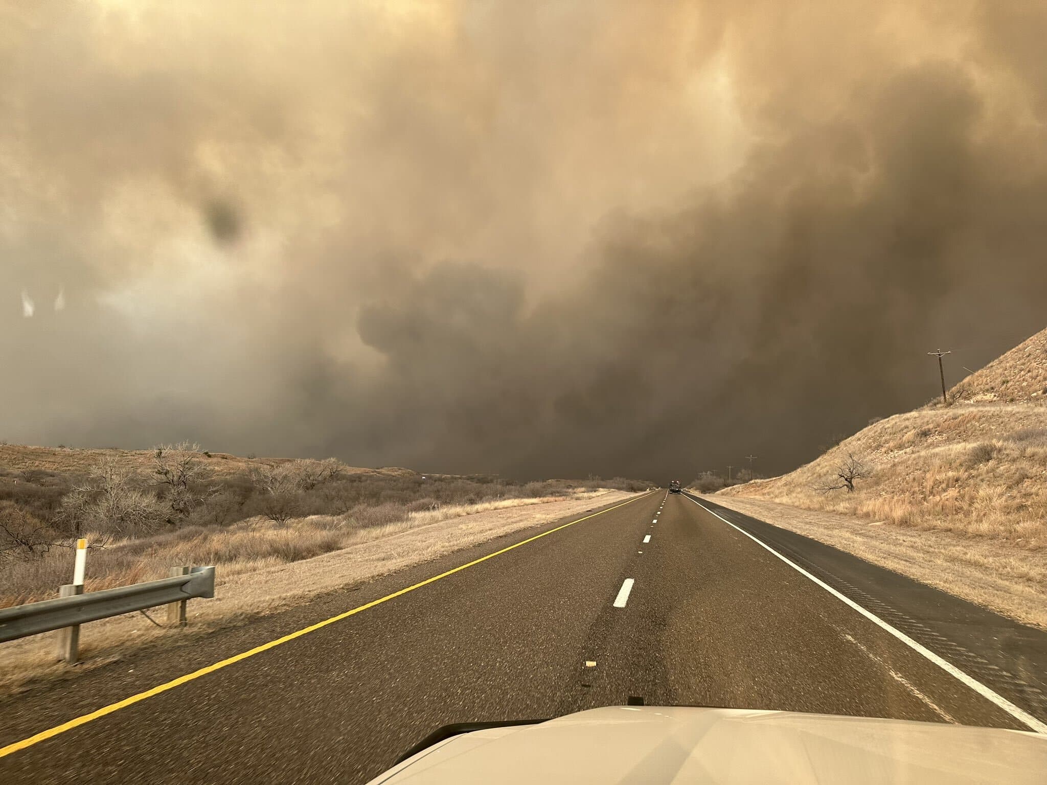 Smoke smothers the horizon on the road ahead, as seen from the dashboard of a truck