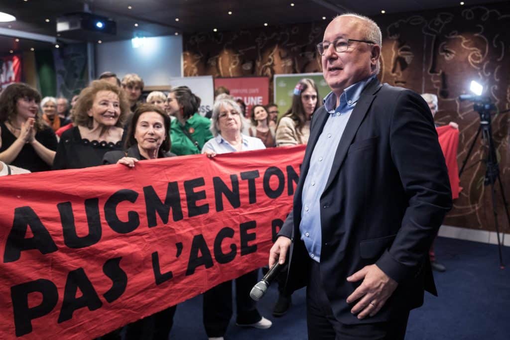 People stand behind a banner as a man walks in front of them