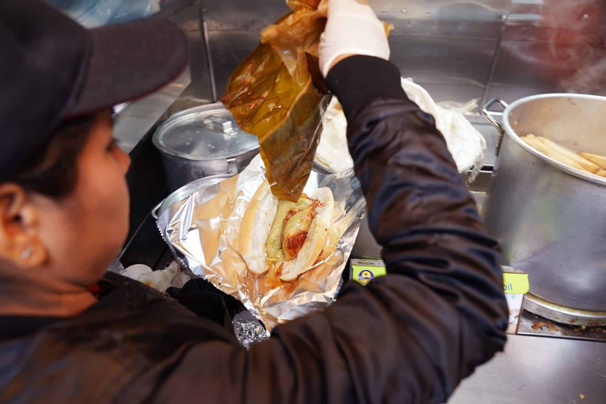 A chef puts a tamale between two buns