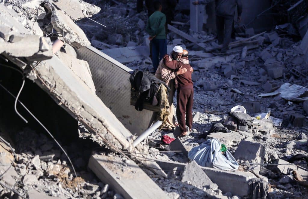 Two Palestinian men embrace among the rubble of their homes